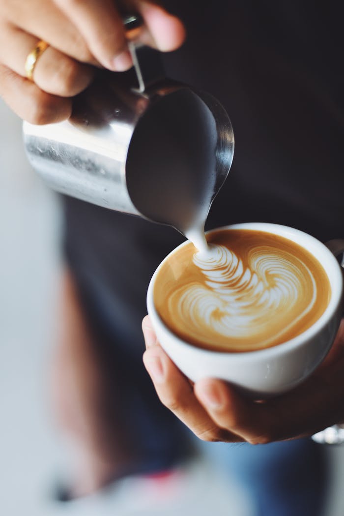 Close-up of hands pouring milk to create latte art in a coffee cup.